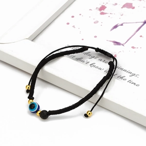 Detail of hand-woven black cord bracelet with blue evil eye bead and lava stone charm
