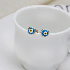 Detail of gold-plated Evil Eye stud earrings hanging on a white ceramic mug rim
