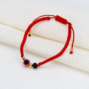 Detail of red braided cord bracelet featuring evil eye bead and black lava stone