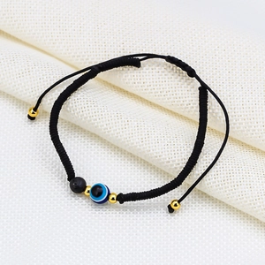 Detail of adjustable woven cord bracelet with blue evil eye charm and black lava stone