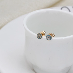 Detail of round bohemian stud earrings with blue stones and white zircon on a ceramic cup