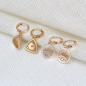 Detail of gold-plated geometric earring set featuring triangle and sunburst eye charms