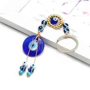 Blue glass Turkish Evil Eye pendant with golden beads and woven cord hanging on white background