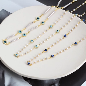 Gros plan de colliers œil maléfique avec perles blanches et maillons dorés sur plateau céramique