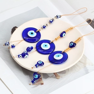 Detailed close-up of three Evil Eye glass charms with golden braided ropes in a white dish