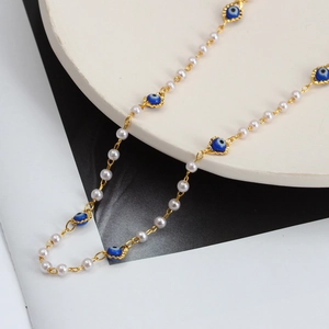 Détail du collier en chaîne dorée avec perles blanches et pendentifs œil maléfique bleus