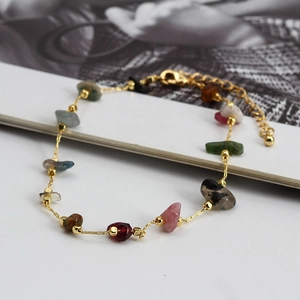 Close-up of multicolor gravel stones and golden chain bracelet with lobster clasp