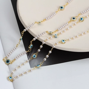 Détail du collier de perles blanches avec pendentifs Œil de Mauvais et touches dorées
