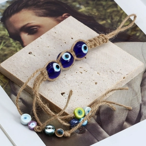 Detail of hand-woven Evil Eye glass beads and braided hemp rope on a textured stone plate
