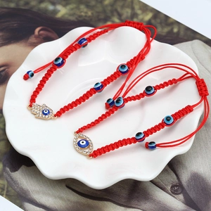 Close-up of red braided bracelets with Hamsa Hand and blue Evil Eye charms on white plate