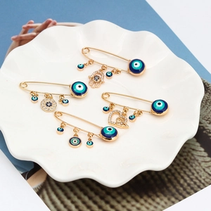 Détail de broches œil protecteur dorées avec pendentifs en cristal sur plateau blanc