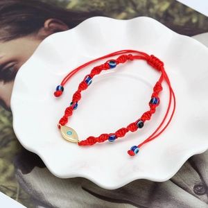 Detailed close-up of a red woven Evil Eye bracelet on a white ceramic dish