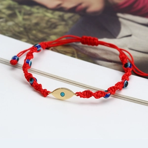 Detail of red braided evil eye bracelet with golden eye pendant and blue beads