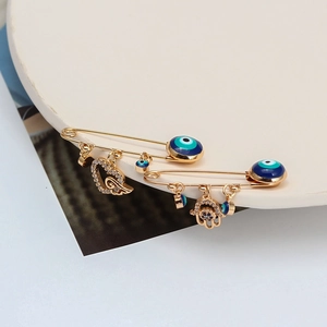 Détail de broches épingles dorées avec œil bleu, main de Hamsa et breloques coeur