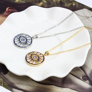 Détail de pendentifs œil maléfique or et argent avec zircons sur une assiette blanche