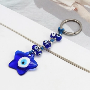 Detailed close-up of blue glass evil eye star keychain with silver beads on white background