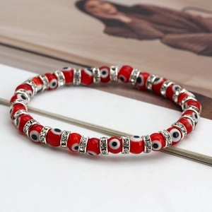 Detail of red Evil Eye beaded bracelet with silver rhinestone spacers on white surface
