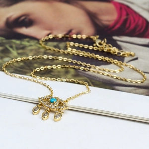 Détail macro du collier avec pendentif œil maléfique doré, pierre turquoise et cristaux