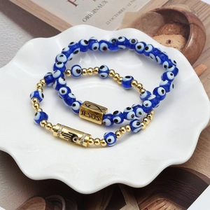 Close-up of Evil Eye beaded bracelets with Jesus and Hamsa Hand charms in a ceramic dish