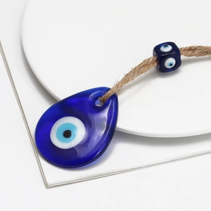 Handmade Evil Eye keychain with blue teardrop glass and woven rope on white tray
