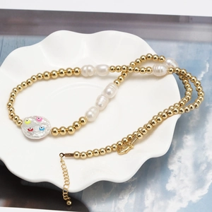 Collier en perles baroques et billes dorées avec pendentif mauvais œil sur plat blanc
