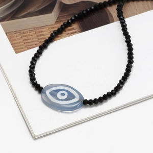Close-up of black faceted beads and light blue evil eye charm on a dainty necklace