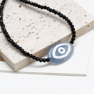 Minimalist evil eye necklace featuring faceted black beads and blue eye charm on stone
