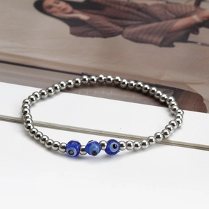 Silver beaded bracelet with blue evil eye charms on a soft fashion background