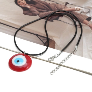 Κοντινό πλάνο κόκκινου μενταγιόν Evil Eye με ζιργκόν σε μαύρο πλεκτό κορδόνι λαιμού