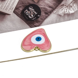 Detail showing pink heart-shaped evil eye pendant with golden metal edge on white paper