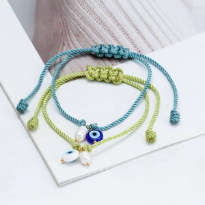 Detail of woven bracelets with evil eye beads and irregular pearls on a white background