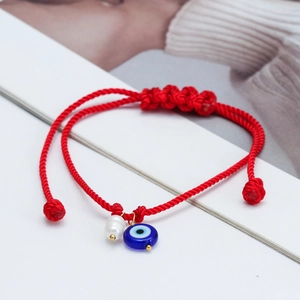 Detailed close-up of a red woven rope bracelet featuring a blue evil eye and pearl charm