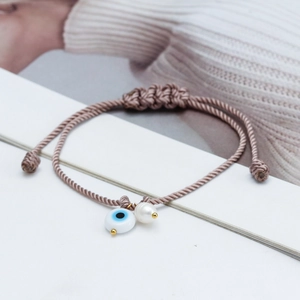 Close-up of adjustable woven evil eye bracelet with a white freshwater pearl charm