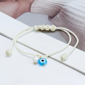 Detail of cream woven cord bracelet with blue evil eye bead and white baroque pearl