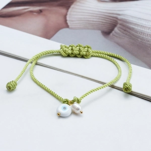Close-up of green woven bracelet featuring blue evil eye bead and baroque pearl detail