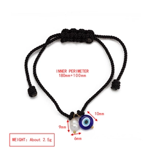 Detailed view of woven black cord bracelet with blue evil eye bead and white pearl charm