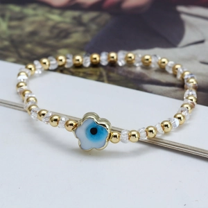 Détail d'un bracelet en perles dorées et cristaux avec un pendentif œil porte-bonheur