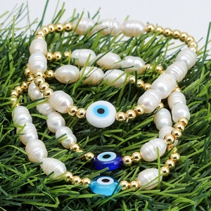 Three-piece set of pearl and evil eye beaded bracelets on a natural green grass background