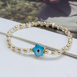 Gros plan sur un bracelet en perles dorées avec cristaux et breloque fleur œil protecteur