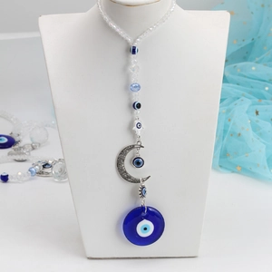 Detail of evil eye moon pendant with blue glass beads and hamsa hand on a white display stand