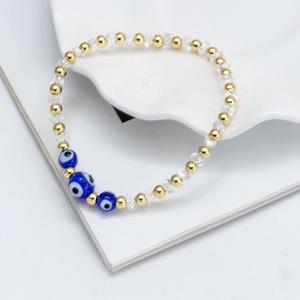 Détail d'un bracelet en perles dorées avec charmes mauvais œil bleu sur fond blanc