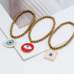 Détail de trois bracelets en perles dorées avec des breloques œil porte-bonheur en émail coloré