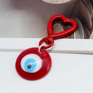 Detail of red heart-shaped spring clasp and circular evil eye pendant on a keychain