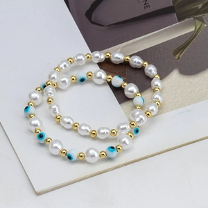 Detail of two-piece elastic beaded bracelets featuring white baroque pearls and evil eye charm