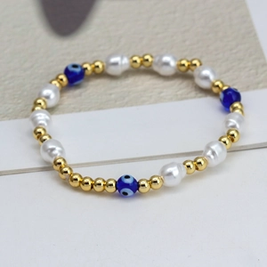 Detail of beaded bracelet with golden beads, white pearls and blue evil eye charms