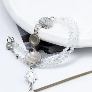 Macro view of double-layered crystal bead bracelet with Hamsa Hand and flower charms