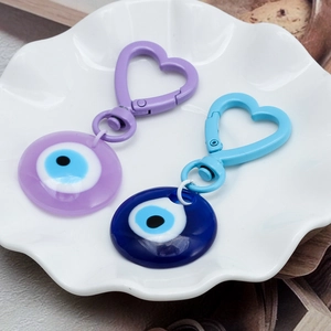 Detail of heart-shaped carabiner and resin evil eye charms in purple and dark blue