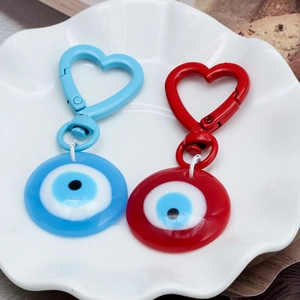 Blue and red heart-shaped evil eye keychains displayed on a white decorative plate