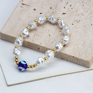 Detailed close-up of blue evil eye bead and white baroque pearls on a stone plate