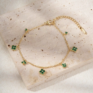 Detalle de pulsera de trébol dorado con circonitas verdes sobre fondo piedra
